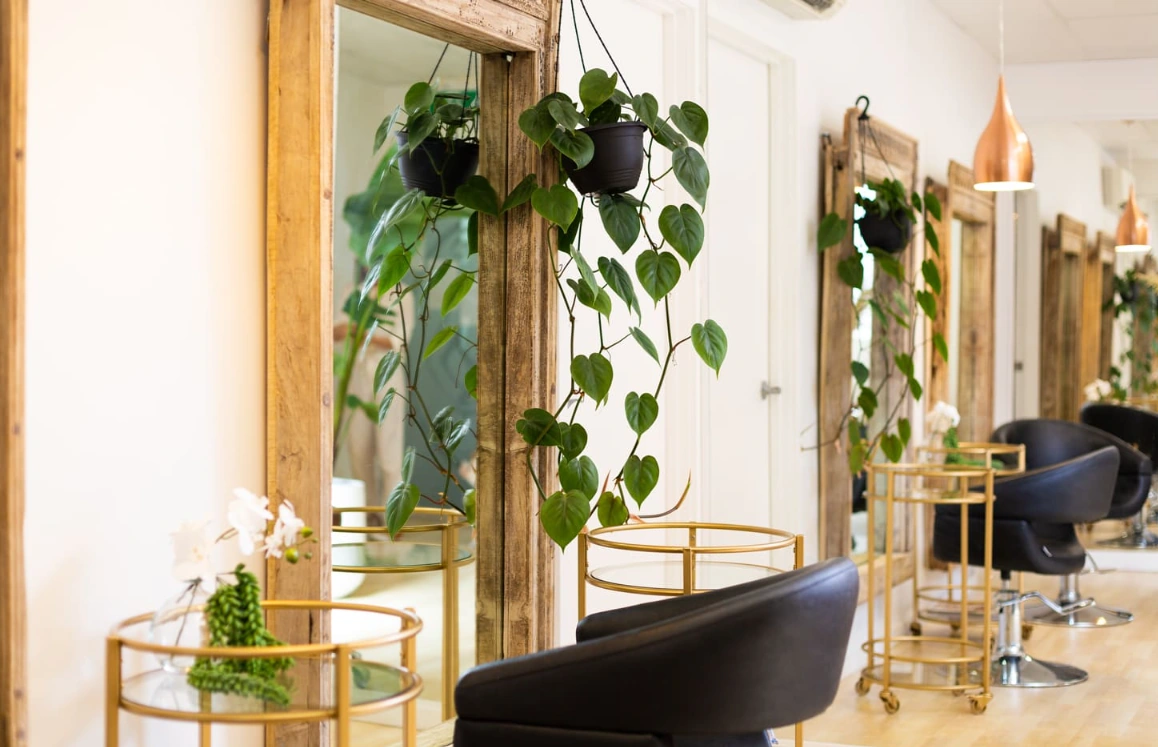 Warm natural light falls across the Noosa Headz salon, with wooden mirrors, leafy plants and black styling chairs